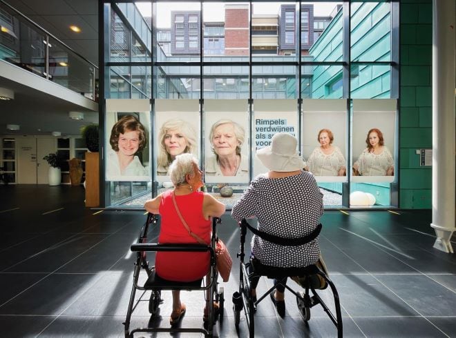 twee dames zittend op hun rollator kijken naar de portretfoto's die gemaakt zijn door fotograaf Marcel de Buck