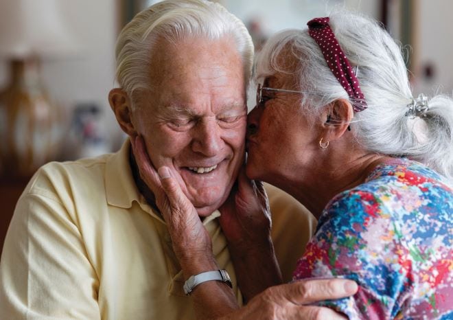 Twee ouderen waarbij de vrouw de man een kus op de wang geeft
