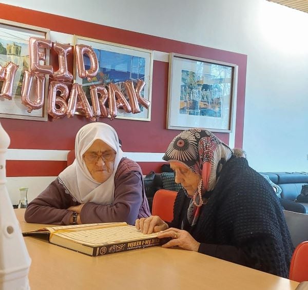 Twee oudere Turkse dames lezen een boek aan tafel