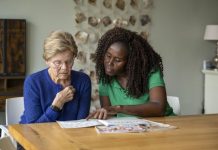 Verzorgende leest samen met oudere dame aan tafel een tijdschrift